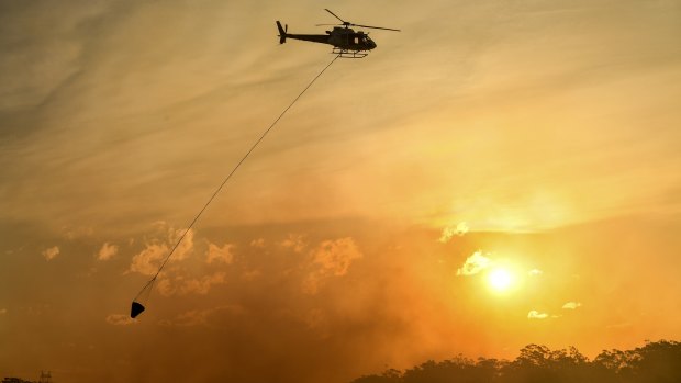 A helicopter water bombs a bushfire threatening homes in Sydney's south-west.