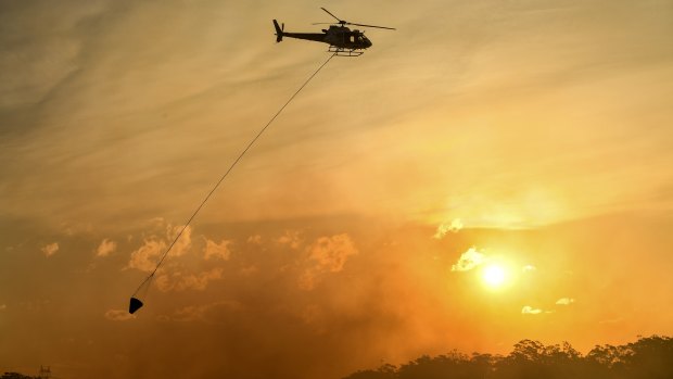 A helicopter water bombs a bushfire threatening homes in Sydney's south-west.