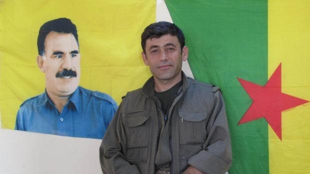 Commander Badr Khan standing under a flag featuring the image of Abdullah Ocalan, the imprisoned PKK leader.