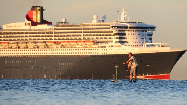 A paddle boarder stays out of the shadow of the Queen Mary II docked at Station Pier.