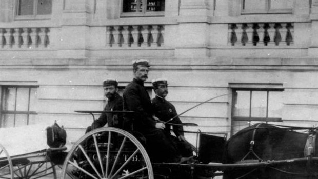 Ambulance officers posing on a buggy with a wheeled litter attached to it.