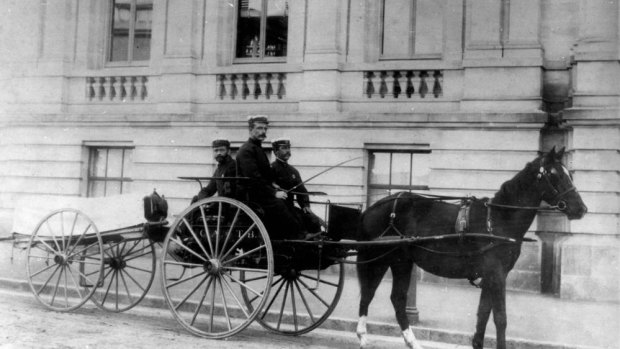 Ambulance officers posing on a buggy with a wheeled litter attached to it.