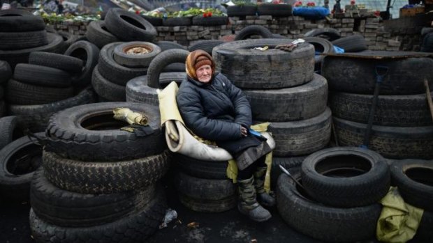 An elderly woman sits on tyres at a barricade in Independence Square.