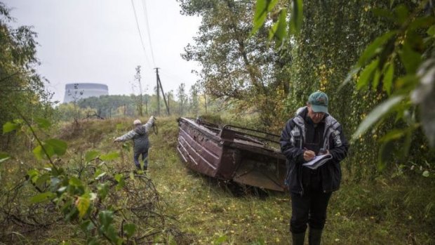 A cooling tower of the Chernobyl Nuclear Power Plant emerges from the forest in the distance as Timothy Mousseau, a biologist, right, measures bat sounds with his assistant.