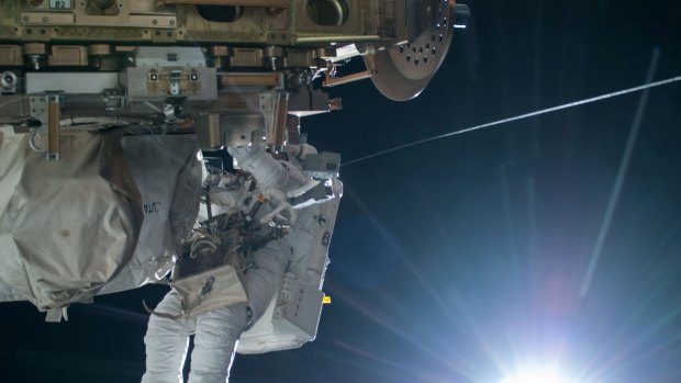 NASA astronaut Terry Virts is seen working to complete a cable routing task while the sun begins to peak over the Earth's horizon on the International Space Station.