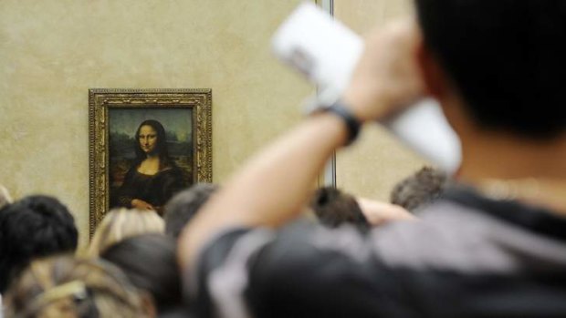 A tourist takes souvenir photos of Italian painter Leonardo da Vinci's famed portrait Mona Lisa at the Louvre Museum in Paris.