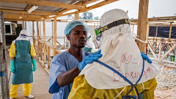 A health care worker prepares a colleague's protective gear at an Ebola virus clinic operated by the International Medical Corps.