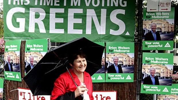 Labor minister Bronwyn Pike is overshadowed by the posters of her Greens opponent as she campaigns in the rain outside a polling place in Carlton yesterday.