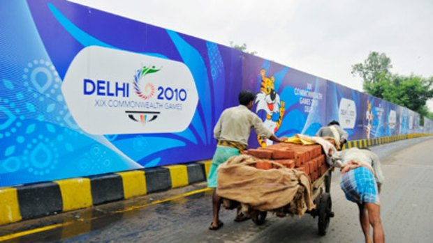 Labourers toil in front of boards advertising the Commonwealth Games.