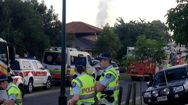 Smoke from a fatal house fire can be seen in the background as emergency workers look on.