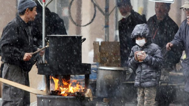 A boy waits for boiled water to cook instant noodle outside a shelter in Sendai, in Miyagi prefecture.