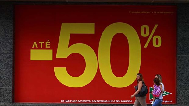 Women walk past a department store announcing discounts of up to 50% before the sales season in Lisbon.