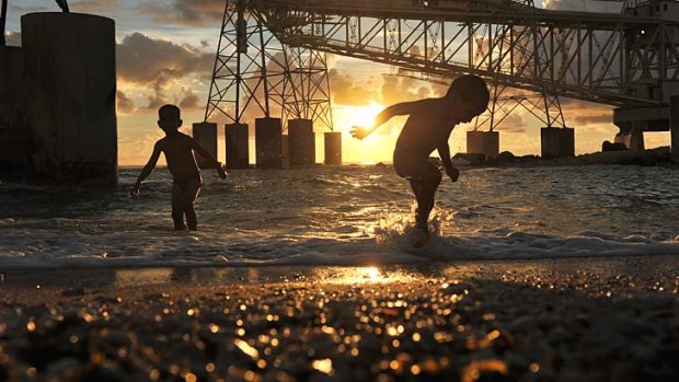Children play at the the water's edge beneath cranes used to load and unload container ships at Nauru, now reinstated as an asylum seeker holding camp.