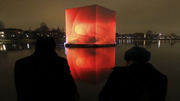 People watch an illuminated so-called CO2 cube is pictured in the water of St Jorgens Lake in front of Tycho Brahe Planetarium in Copenhagen.