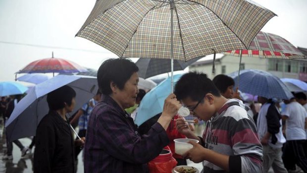 Family support ... a student takes lunch as his grandmother holds an umbrella for him outside a school gate in Hefei, Anhui Province.
