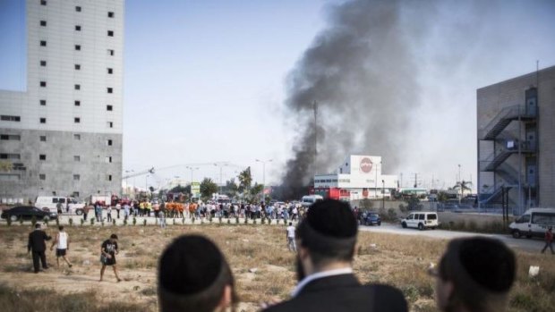 Israelis watch as firefighters try to douse a fire from a rocket that hit a petrol station in the southern Israeli city of Ashdod, wounding three.