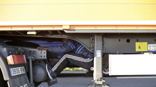 A migrant sits under the trailer of a lorry as he attempts to cross the English Channel, in Calais, northern France on Wednesday.