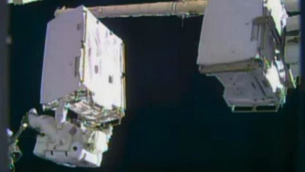 Astronaut Mike Hopkins on the robotic arm holding a spare pump to change for a problematic pump during a spacewalk outside the International Space Station.