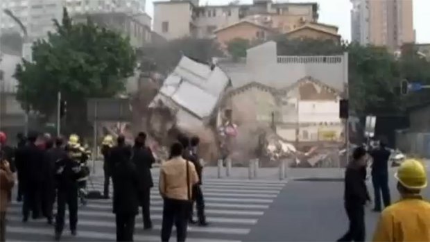 Collateral damage ... A three-storey building next door also collapses into the giant hole as bystanders watch.