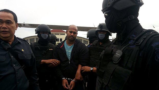 Myuran Sukumaran is surrounded by masked security personnel upon arriving at Cilacap airport.