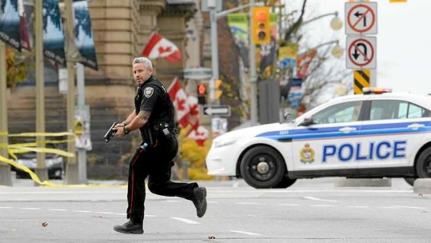 An Ottawa police officer runs with his weapon drawn outside Parliament Hill in Ottawa.