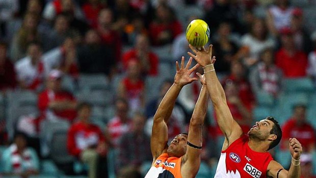 Israel Folau leaps high but finds a much smaller man, Heath Grundy, outdoing his effort during the opening round AFL clash between GWS and Sydney.