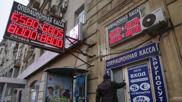 A man walks into a building, past a board showing currency exchange rates in Moscow.