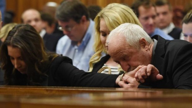 The father of defendant Oscar Pistorius, Henke (right), kisses the hand of his daughter Aimee as  Judge Thokozile Masipa began handing down her verdict.