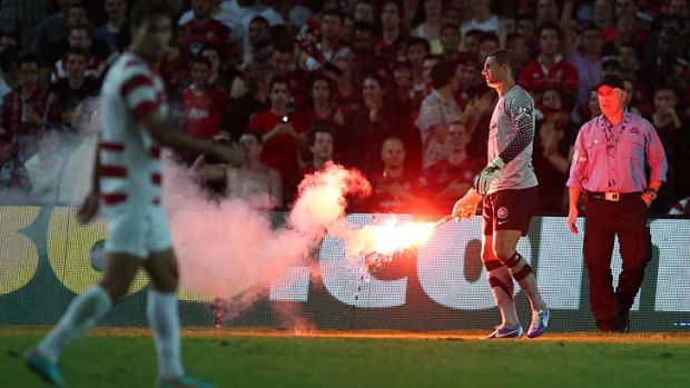 Smoke and ire &#8230; Western Sydney goalkeeper Ante Covic picks up a flare thrown on the pitch during Saturday night's match. Three fans were charged.