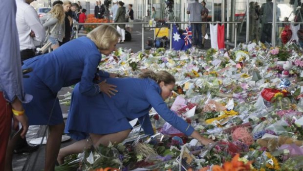 Remembering MH17: Two KLM cabin crew reach out into a sea of flowers at Schiphol airport in Amsterdam.