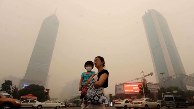 Mystery haze ... a Chinese woman carries her daughter who is wearing a mask as they make their way along a busy intersection in Wuhan, central China's Hubei province.