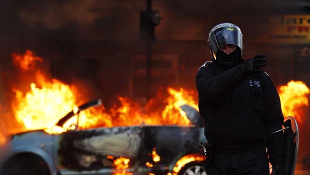 A riot police officer directs his colleagues to clear people away from a burning car in Clarence Road in Hackney.