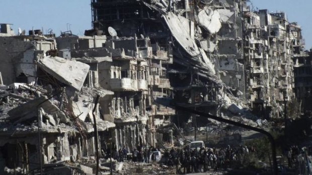 Destruction: People waiting to be evacuated gather near damaged buildings in Homs.