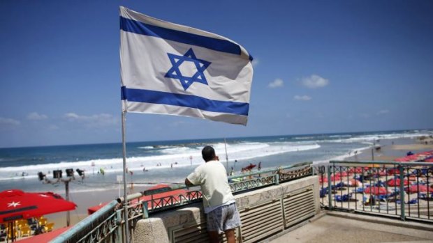 A man looks at the sea as an Israeli flag flutters nearby in Tel Aviv.