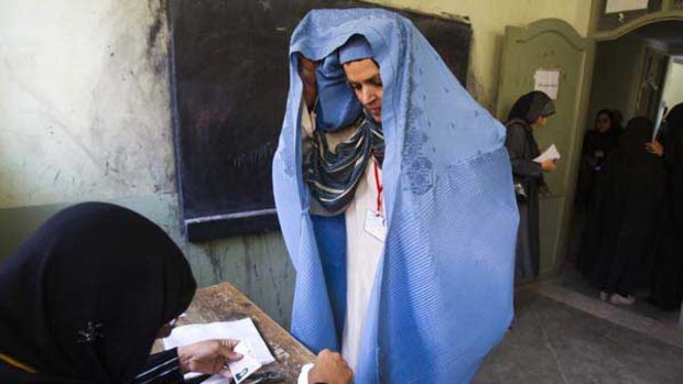 A woman in a burqa shows her face to an election official before casting her ballot at a polling station in Herat, western Afghanistan.