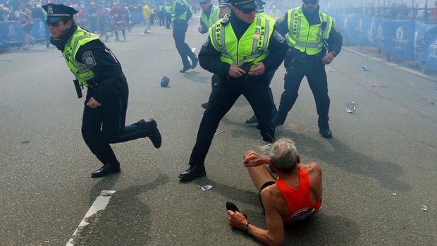 Runner Bill Iffrig, 78, lies on the ground as police officers react to a second explosion at the finish line of the Boston Marathon.