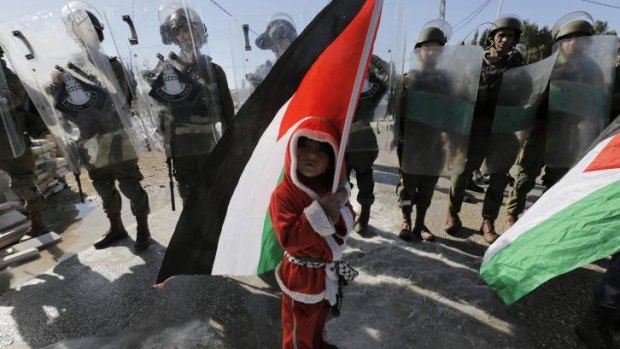 A Palestinian boy dressed as Santa Claus holds a Palestinian flag as he stands in front of Israeli soldiers during a protest against the controversial Israeli barrier in the West Bank village of al-Masara near Bethlehem.