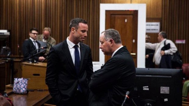 Oscar Pistorius speaks to Kenny Oldwage of his legal team with the reconstructed toilet door in the background.