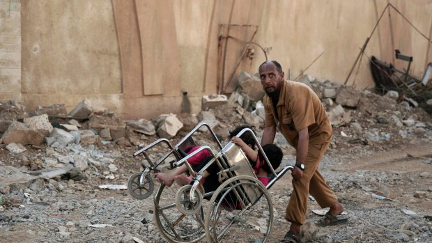 A man pushes two children in a wheelchair as they flee heavy fighting in western Mosul.
