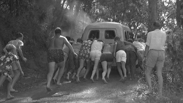 Helpers try unsuccessfully to push the broken-down vehicle up a steep incline.