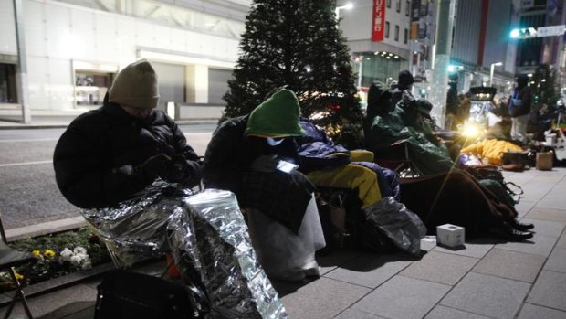 People sit on a street in front of an Apple store in Tokyo.