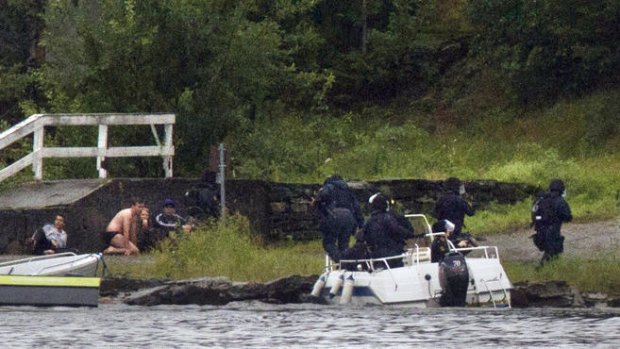 Campers crouch behind a wall on the waterfront of Utoeya Island, north-west of Oslo, as armed police officers arrive by boat to confront the gunman.
