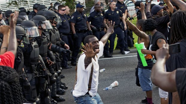 A man attempts to stop protesters from engaging with police in riot gear in front of the Baton Rouge Police Department headquarters.