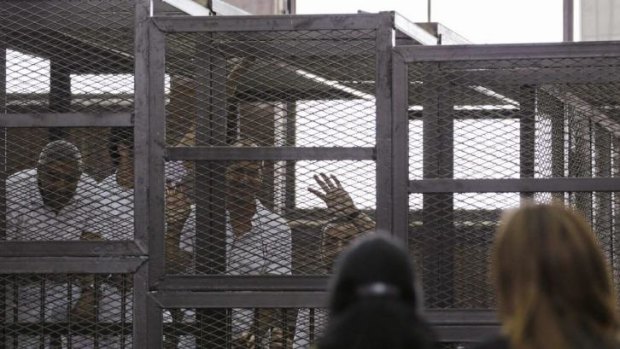 Al Jazeera journalists (left-to right) Mohammed Fahmy, Peter Greste and Baher Mohamed wave to a friend and Fahmy's fiancee as they stand behind bars in a court in Cairo. 