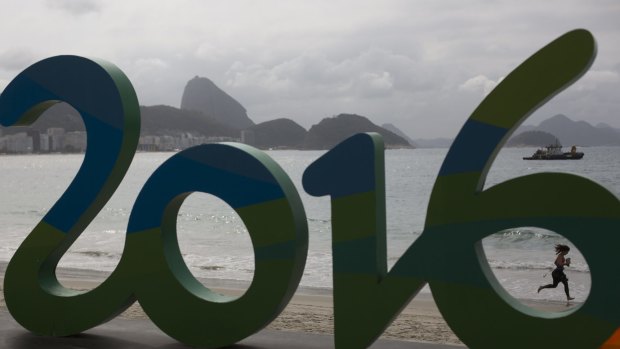 A woman runs past a Rio 2016 sign backdropped by Sugarloaf mountain at Copacabana beach in Rio de Janeiro.