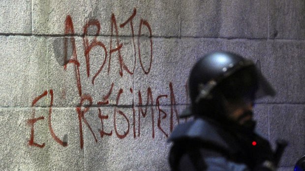 A member of the riot police stands near an inscription that reads 'down with the regime' during a Madrid protest against education spending cuts.