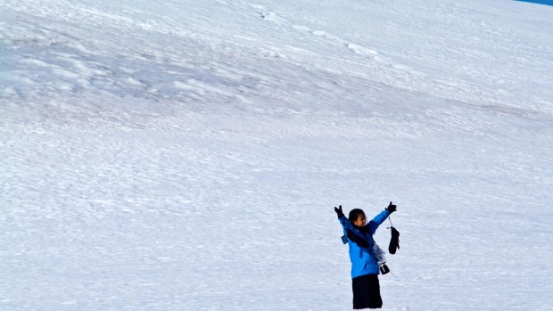 A tourist on a snowy mountainside celebrates being in Antarctica. 