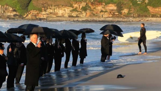 Formally suited volunteers in bowler hats and with umbrellas take part in the human sculpture at dawn on Bondi Beach.
