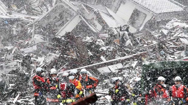 Rescuers search for bodies through the snow in the rubble of Minamisanriku.