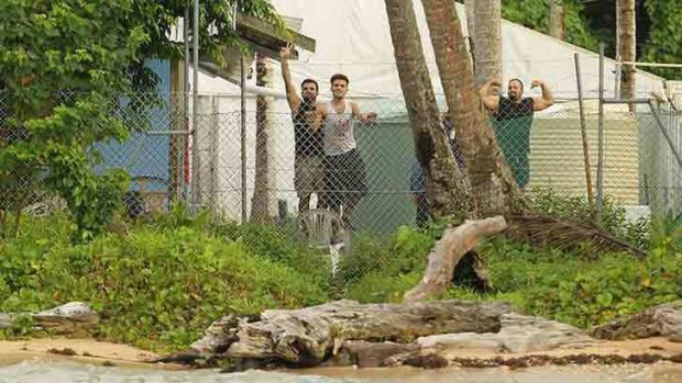 Asylum seekers wave from behind the wire of the Manus Island detention centre.